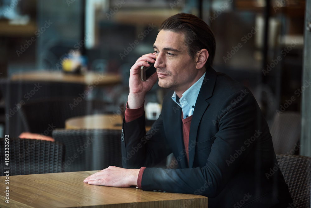 Poster side view smiling male speaking by mobile while locating at desk in cafe. conversation and rest conc