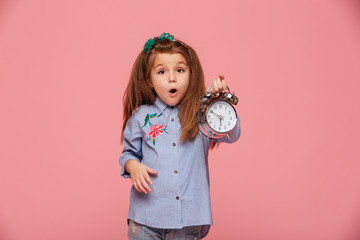 Shot of female kid posing on camera with eyes and mouth wide open holding clock nearly 6 being...