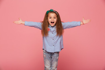Cheerful little girl in hair hoop posing with open hands against pink background being friendly and welcoming