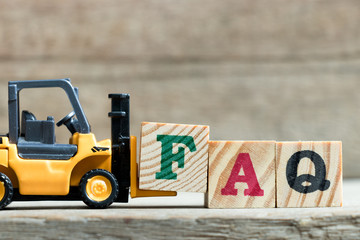 Toy yellow forklift hold letter block F to complete word FAQ (Abbreviation of Frequently asked...