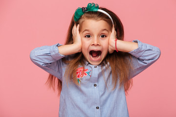 Surprised little girl covering her ears with both hands not listening or overhearing screaming with...