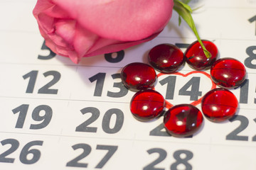 The concept of Love, St. Valentine's Day with a beautiful pink rose on a calendar, February 14th marked with a heart and red glass pebbles