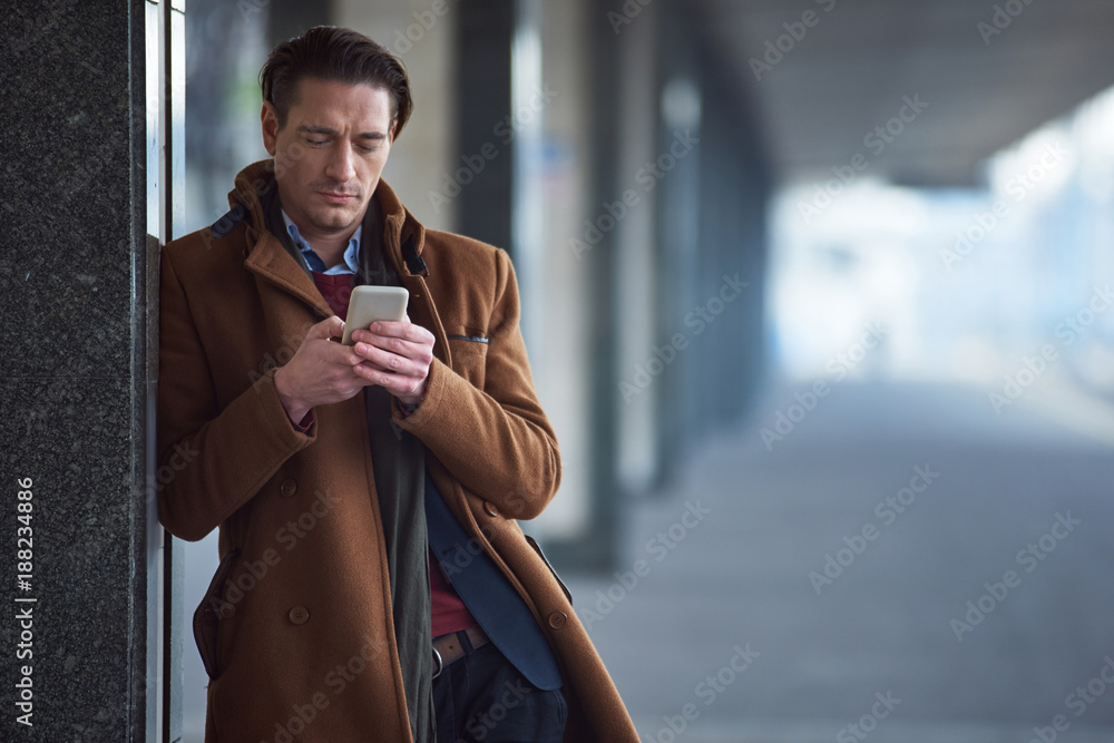 Aufkleber portrait of serene male sending message by mobile while situating in railway station. gadget concept