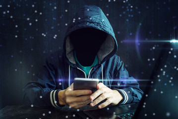 An anonymous hacker without a face uses a mobile phone to hack the system. The concept of cyber...