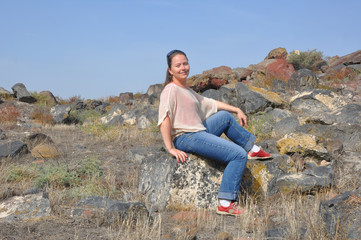 Naklejka na ściany i meble Smiling woman sitting on stones