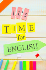 Learning Foreign Languages concept: It's Time For English inscription and bright school supplies on a light colored wooden background, close up, top view