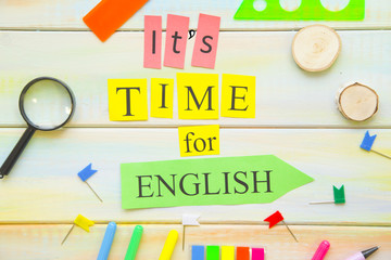 Learning Foreign Languages concept: It's Time For English inscription and bright school supplies on a light colored wooden background, close up, top view