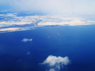 Japan Sendai bay, city, seashore, and port in winter, covering with white snow field, large deep blue sea water surface area below background, foggy cloud, high top view from 3000 feet flying aircraft