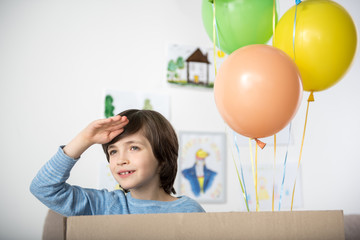 Portrait of smiling boy holding his hand near his forehead and peering into distance joyfully. Air...