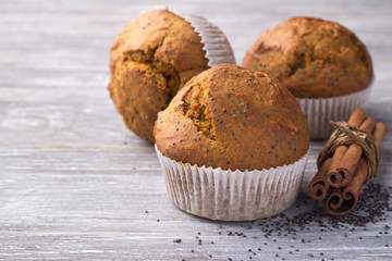 Three delicious homemade pumpkin muffins with cinnamon and poppy seeds on wooden surface, top view, selective focus