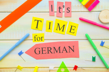 Learning Foreign Languages concept: It's Time For German inscription and bright school supplies on a light colored wooden background, close up, top view