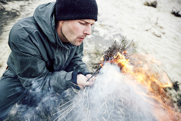 Young man kindles fire, with burning fire in his hand