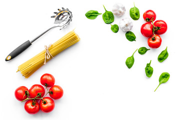 Cooking italian pasta. Spaghetti, tomatoes, garlic, basil and cookware on white background top view copy space