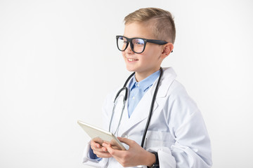 Smiling boy playing game as if he is examining a patient in the hospital. He is holding tablet. Copy space in left side. Isolated on background