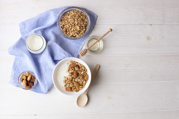 Ceramic bowl of Greek yogurt and mixed nuts. Nutritious vegetarian protein rich diet homemade breakfast with almond milk, cashew, hazelnut, rolled oats on white table. Top view, background, copy space