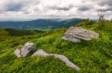 Fototapeta na wymiar grassy slopes of Carpathian mountains. huge boulder on the edge of a hill side. mountain ridge under the cloudy sky in summer time