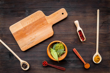 Mock up for menu or recipe. Wooden cutting board near scoops and spoons with spices on dark wooden background top view