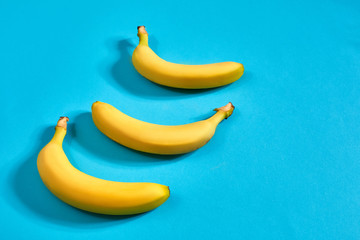 Three yellow ripe bananas on blue background with space for text or design. Top view