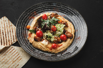 Hummus with vegetables and seafood on black background