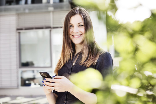 junge Frau mit ihrem Smartphone auf einer begrünten Terrasse eines Bürogebäudes,Köln, 
