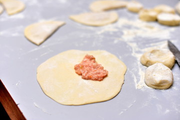 Chebureks. Cook at home. Not roasted cheburek with flour on a wooden board. Single round piece of dough folded over the filling in a crescent shape. Dish of the Crimean Tatars and for the Caucasian