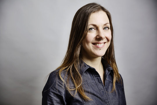 junge Frau mit langem Haar und Piercings im Gesicht, Portrait vor grauem Hintergrund