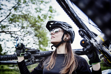 junge Bikerin trägt ihr Mountainbike auf der Schulter - obrazy, fototapety, plakaty