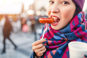 young woman traveler snacks a sausage with a hot drink on the street of a European city in the...