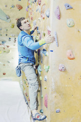 Young man practicing rock-climbing on a rock wall indoors.