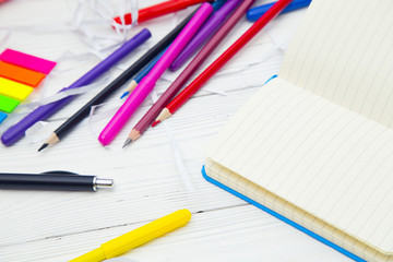 Education and creativity concept. A blank notebook, colored pencils and markers on a white wooden table, space for a text or product display