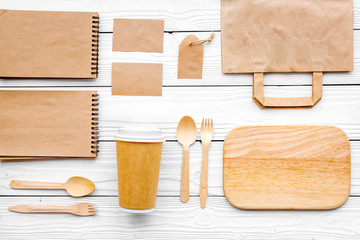 Set of recycle brown paper bag, disposable tableware cup, spoon, fork, notebook on white wooden background top view pattern mockup