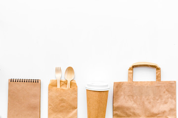 Disposable tableware. Paper cup, spoon, fork near brown paper bag and notebook top view copy space...