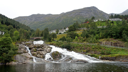 View of waterfall in Hellesylt, small town at the entrance to Geirangerfjord on a summer day, mountain in the background, More og Romsdal, Norway