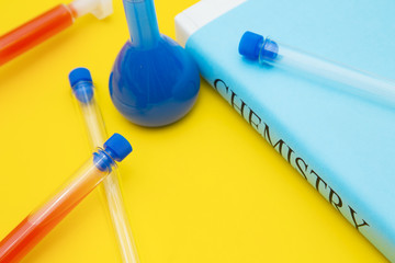 Education concept: Chemistry student's book in a blue cover, chemical flasks and test tubes with red and blue liquid on a bright yellow background with copy space