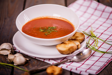 tomato soup  with pasta and chives and bread crouton in white plate on wood table 