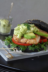 schwarzer Burger mit Hühnchenfleisch, Rucola, Avocado, Tomate und Avocadocreme