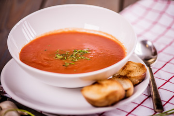 tomato soup  with pasta and chives and bread crouton in white plate on wood table 