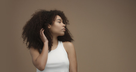 mixed race black woman portrait with big afro hair, curly hair in beige background Touching her hair