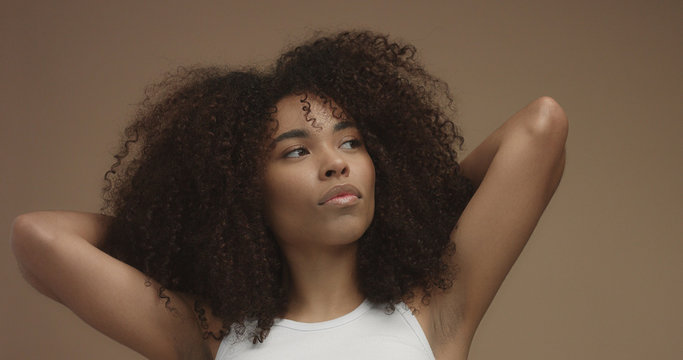 mixed race black woman portrait with big afro hair, curly hair in beige background Dancing closeup