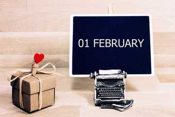 Wooden cube shape calendar for FEB 1 on green book, table. 