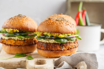 Healthy baked sweet potato burger with whole grain bun, guacamole, vegan mayonnaise and vegetables on a wooden board. Vegetarian food concept, light background. © vaaseenaa
