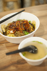 A bowl of delicious noodles with barbecue meat covered with dark soy sauce.