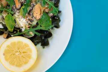 Black pasta with seafood in white cream sauce and lemon. Blue background