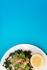 Fototapeta na wymiar Black pasta with seafood in white cream sauce and lemon. Blue background