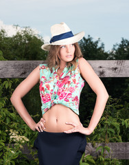 Vertical portrait of a beautiful young woman in hat posing by a wooden fence