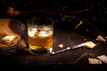 Glass of whiskey with ice cubes served on wooden table.