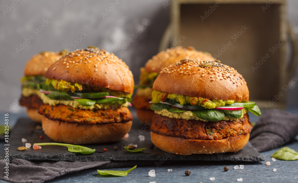 Wall mural Healthy baked sweet potato burger with whole grain bun, guacamole, vegan mayonnaise and vegetables on a black slate board. Vegetarian food concept, dark background.