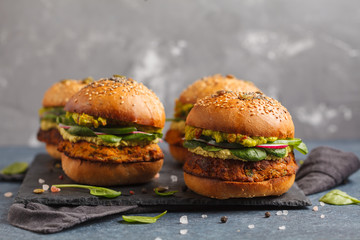 Healthy baked sweet potato burger with whole grain bun, guacamole, vegan mayonnaise and vegetables on a black slate board. Vegetarian food concept, dark background.