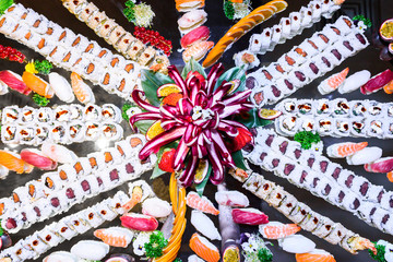 A great composition of many pieces of sushi on a large mirrored plate seen from above. Radicchio like a bouquet of flowers as decoration. Sushi background