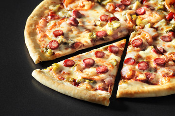 cut Pizza close up with sausages on black stone background